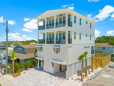 A modern three-story white building with balconies next to "Shore Dogs" restaurant. Palm trees and clear blue sky in the background.