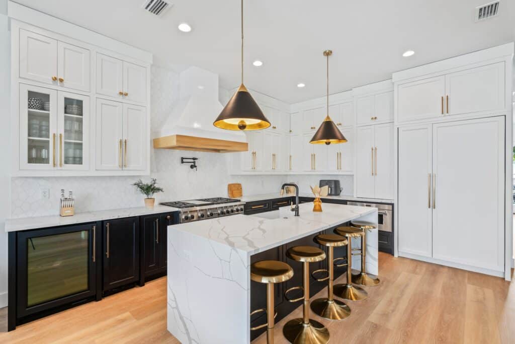 Modern kitchen with white cabinets, marble island, brass fixtures, and black-and-gold pendant lights. Barstools and wood flooring create a stylish contrast. Residential full-service interior design services by Kristin Midgett Design - Santa Rosa Beach, FL.