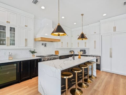 Modern kitchen with white cabinets, marble island, brass fixtures, and black-and-gold pendant lights. Barstools and wood flooring create a stylish contrast. Residential full-service interior design services by Kristin Midgett Design - Santa Rosa Beach, FL.