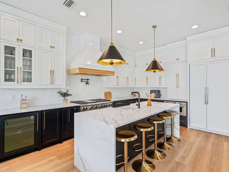 Modern kitchen with white cabinets, marble island, brass fixtures, and black-and-gold pendant lights. Barstools and wood flooring create a stylish contrast. Residential full-service interior design services by Kristin Midgett Design - Santa Rosa Beach, FL.