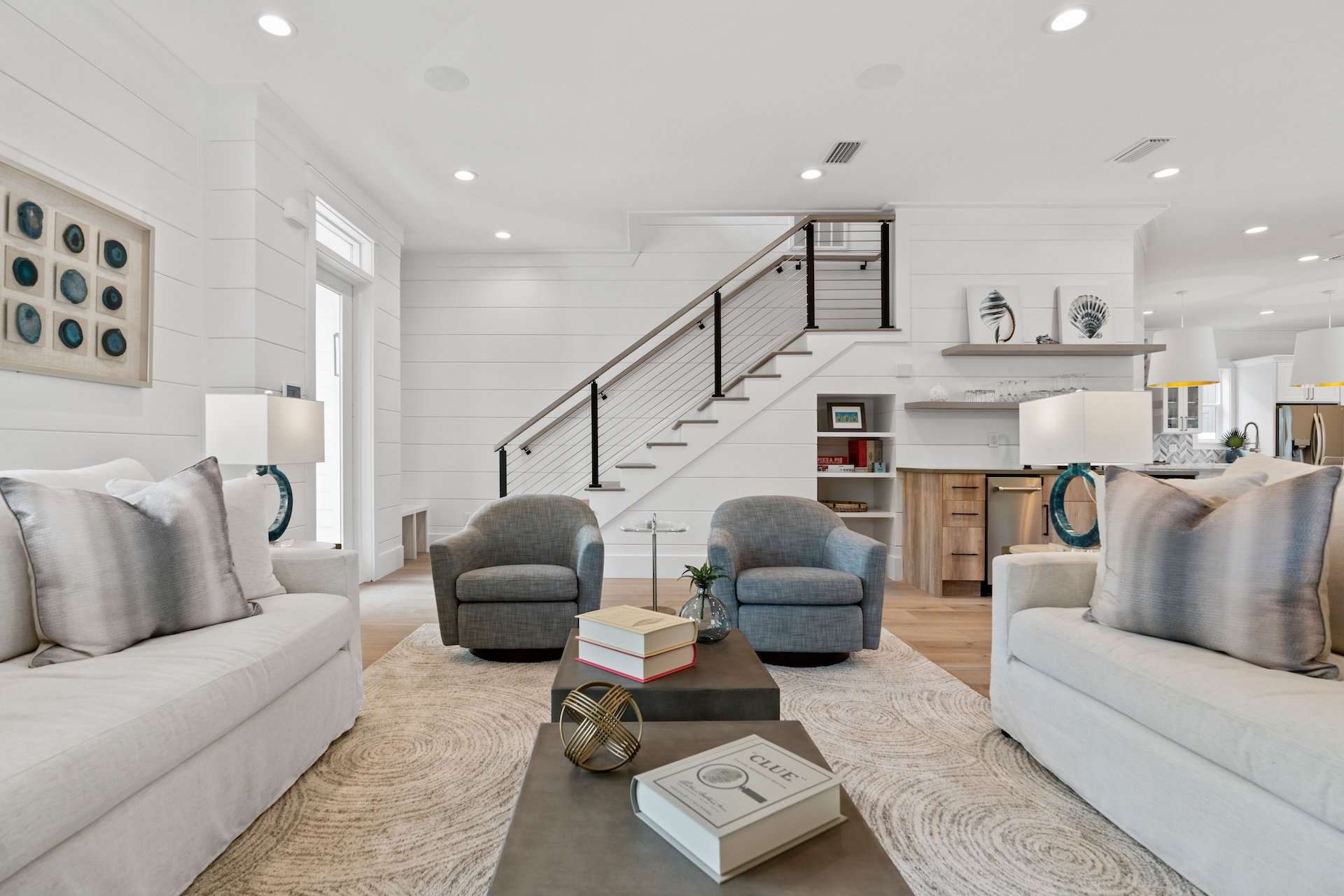 Bright, modern living room featuring cozy furniture, a central coffee table with books, and a staircase with sleek railing design.