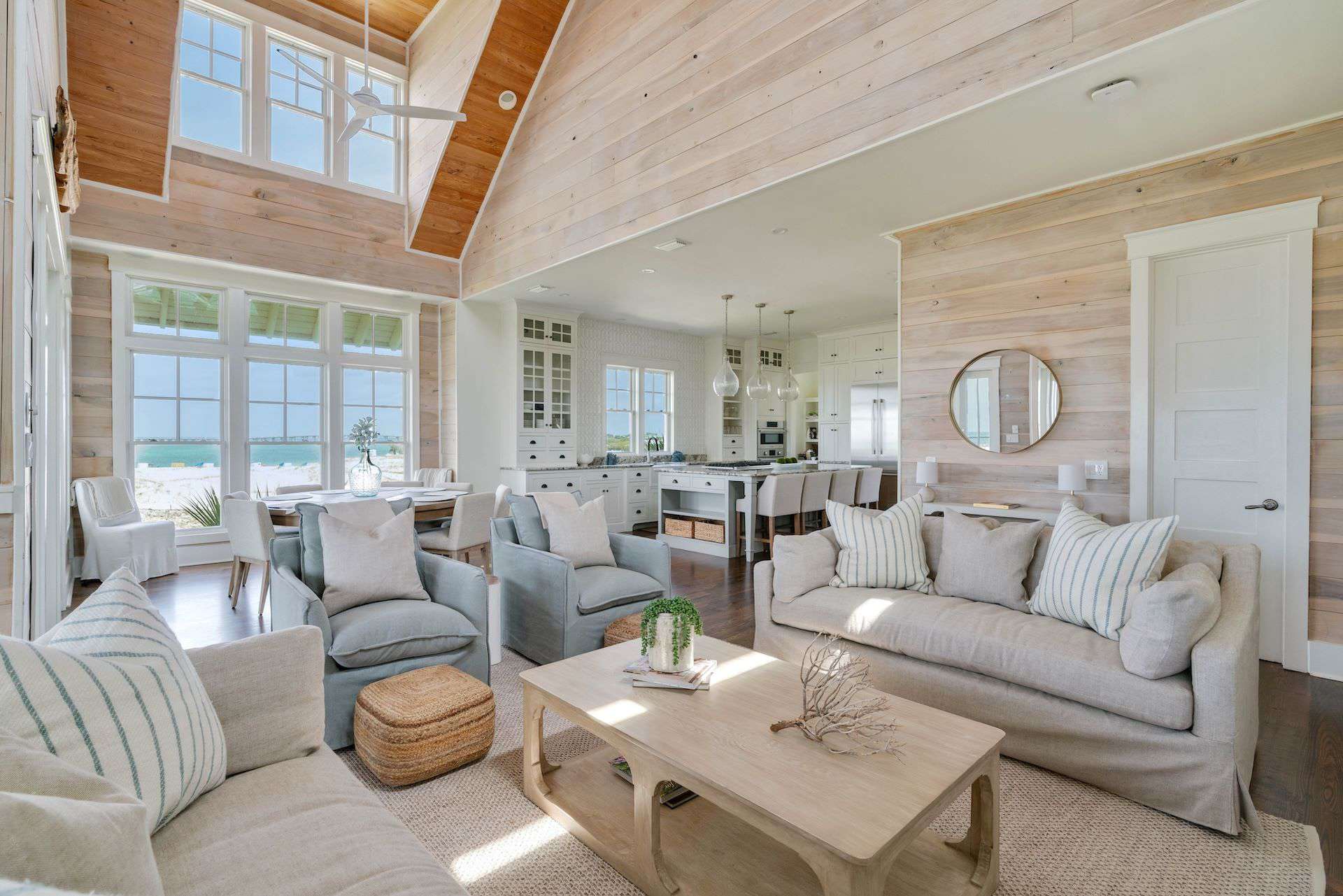 Bright, airy living space with high ceilings, ocean views, plush seating, and modern kitchen in coastal style, featuring wood accents and large windows.