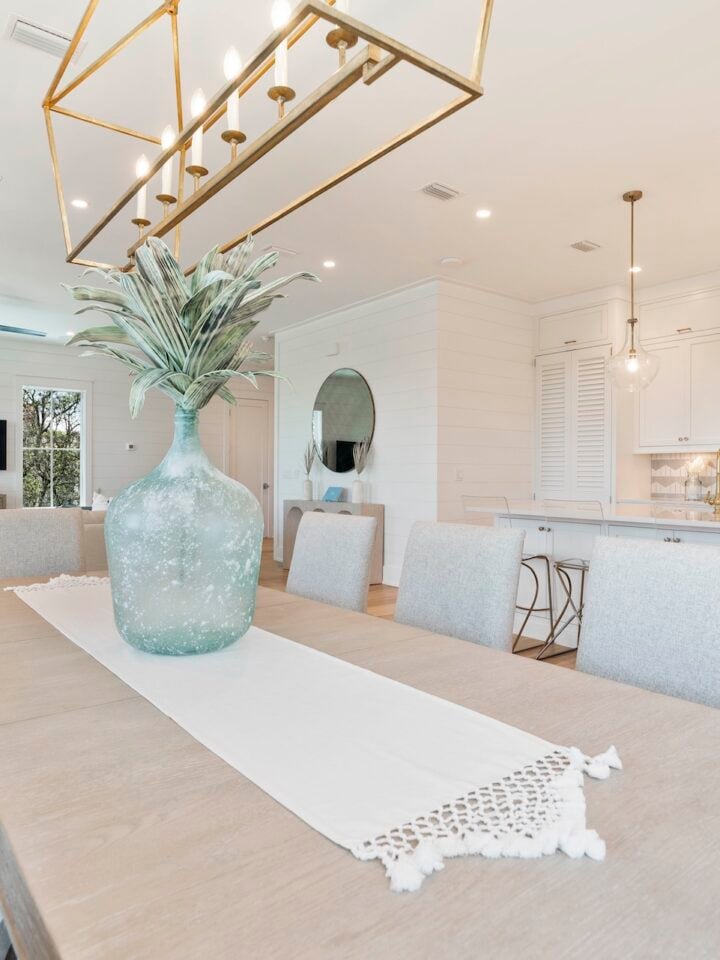 Bright, modern open-concept living and dining area with elegant decor, neutral tones, large table, decorative vase, and stylish pendant lighting. Cozy, inviting atmosphere.