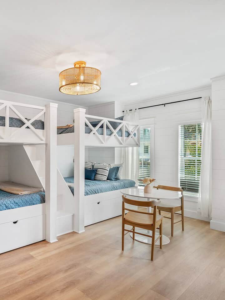 Spacious, modern bedroom with stylish bunk beds, wooden flooring, surfboard decor, and a small table with chairs, accented by natural light and plants.