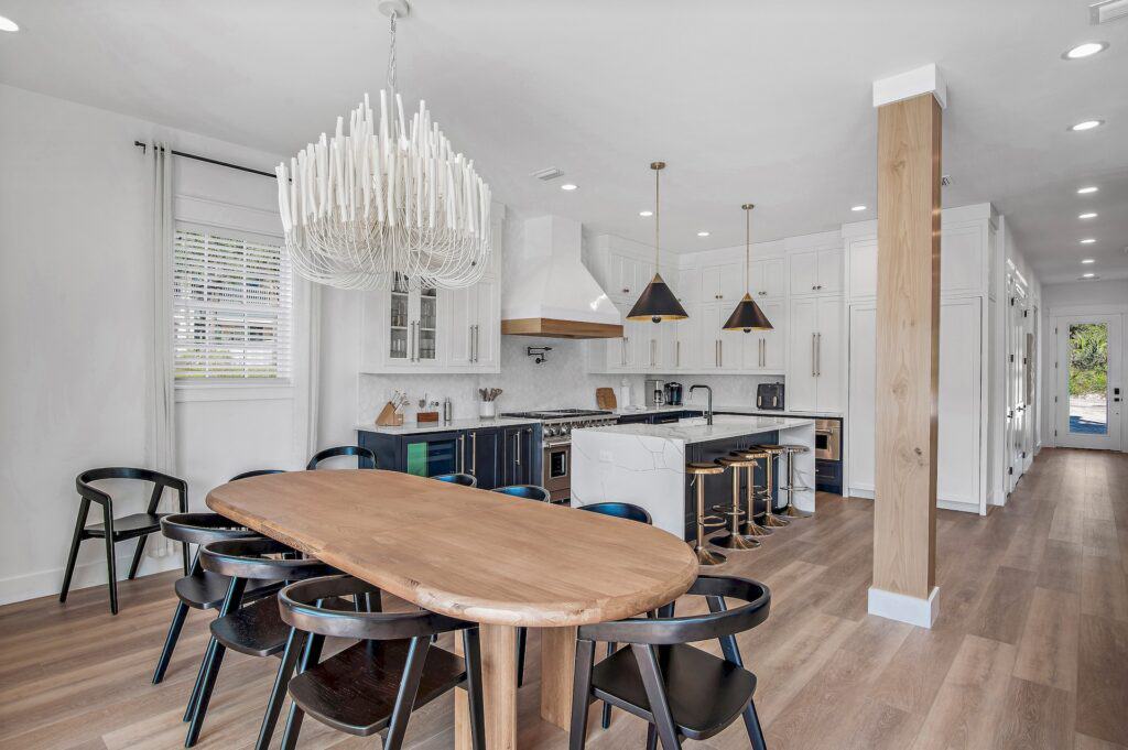 Modern kitchen-dining room with wooden table, black chairs, stylish chandelier, and marble island. Light wood flooring enhances clean, minimalist design.