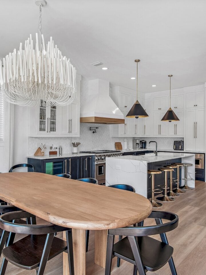Modern kitchen-dining room with wooden table, black chairs, stylish chandelier, and marble island. Light wood flooring enhances clean, minimalist design.