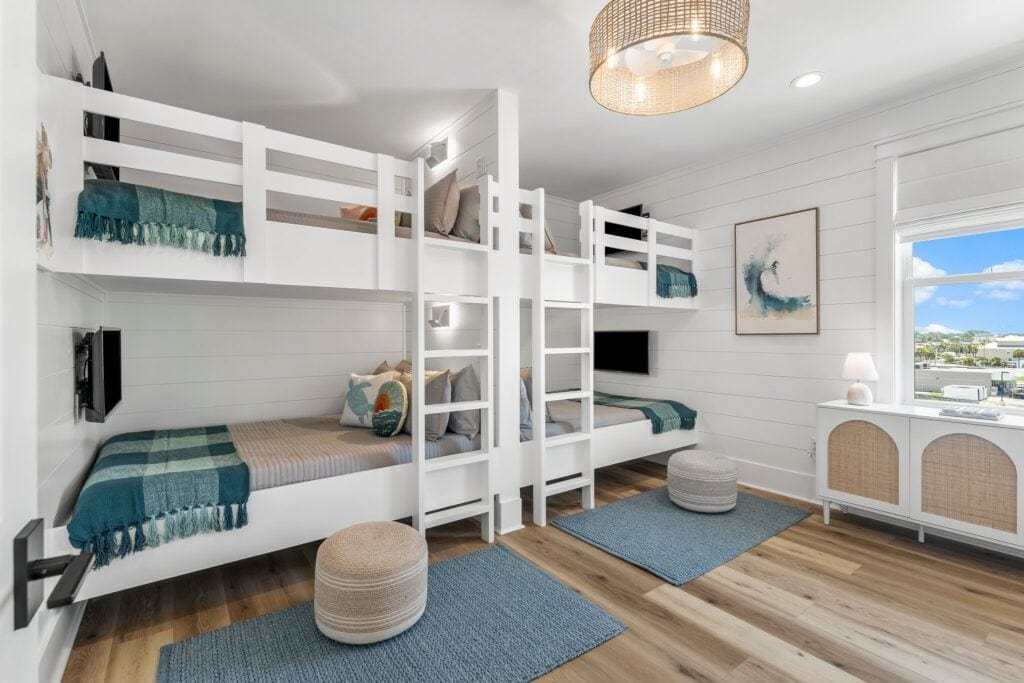 Bright, modern room with white bunk beds, teal accents, and ocean-themed decor. Large window offers city view. Cozy, inviting atmosphere.