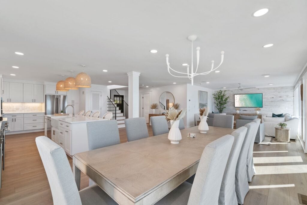 Spacious, modern open-plan kitchen and dining room with white cabinets, wooden floors, island, large dining table, and cozy living area with natural light.