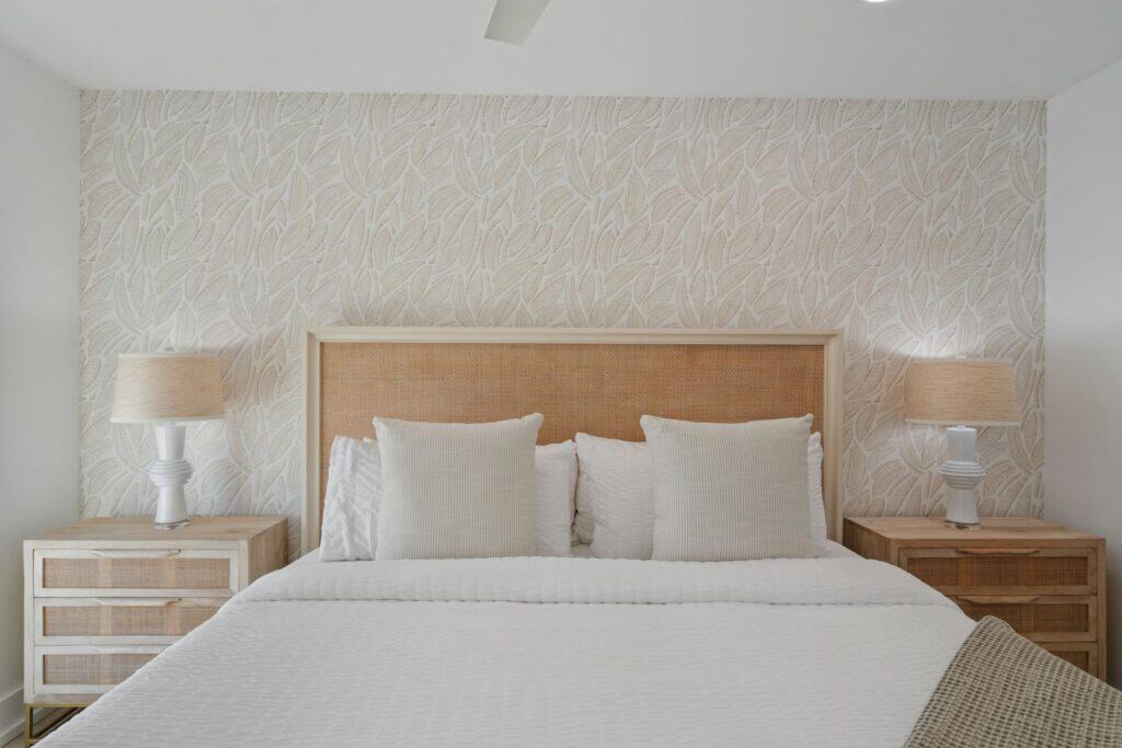 A stylish, minimalist bedroom features a textured headboard, coordinated pillows, bedside tables with lamps, and leaf-patterned wallpaper, creating a serene ambiance.