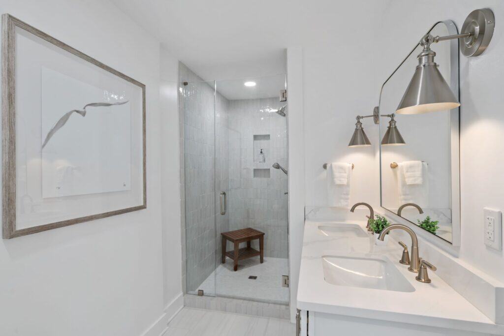 A modern bathroom features a glass shower, dual sinks, elegant fixtures, wall art, and soft lighting, creating a clean, sophisticated atmosphere.