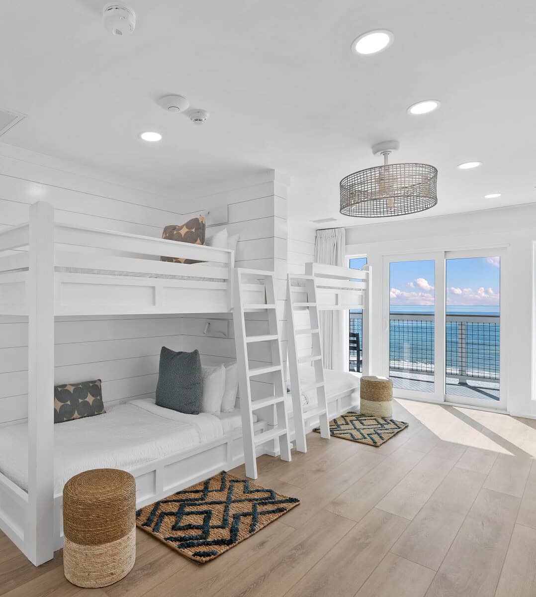 Bright, modern room with bunk beds, wooden flooring, and ocean view. Sliding glass doors lead to balcony; adjacent room visible through open doorway.