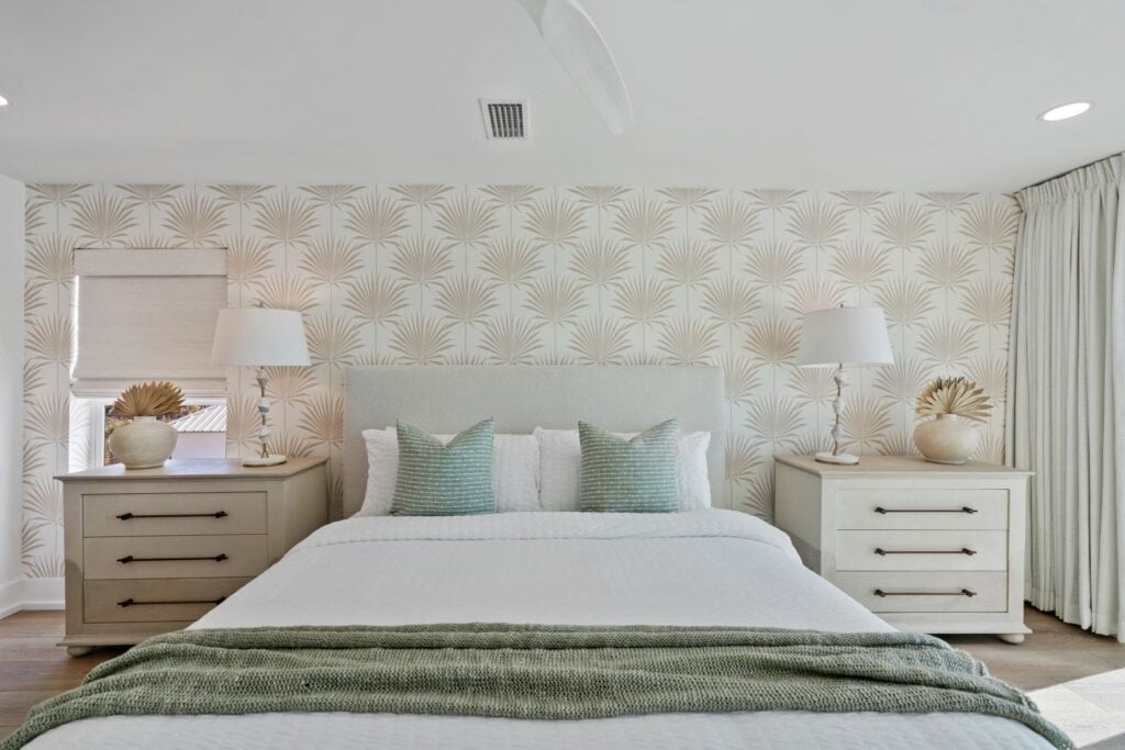 A cozy bedroom features a patterned wallpaper, two nightstands with lamps, and a neatly made bed with green and white pillows.