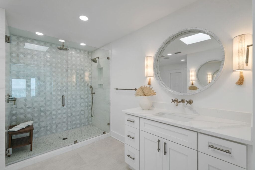 Elegant bathroom with glass shower, white vanity, large round mirror, and soft lighting, creating a modern, serene atmosphere.
