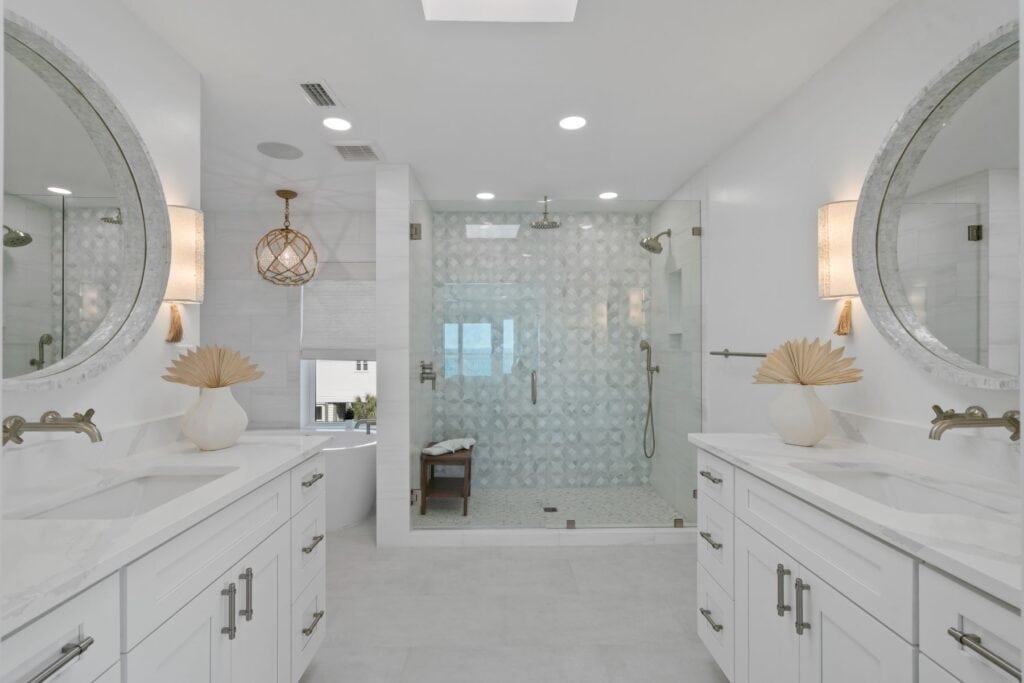 Modern bathroom featuring dual vanities, round mirrors, and a walk-in shower with decorative tiles. Neutral tones and elegant lighting enhance the space.