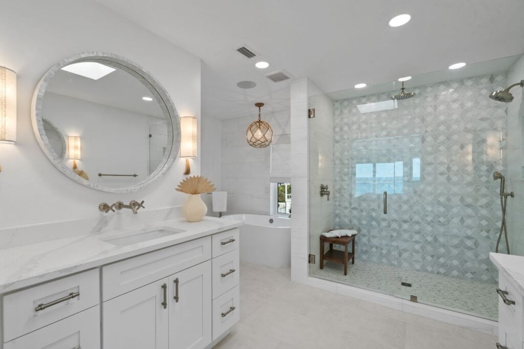 Modern bathroom with large glass shower, round mirror above marble countertop, freestanding tub, decorative lighting, and white cabinetry, creating a spa-like ambiance.