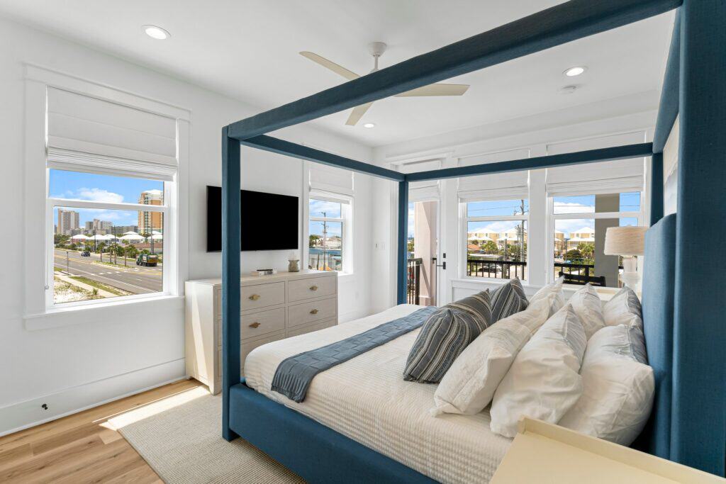 A modern bedroom with a blue canopy bed, multiple windows, and a city view featuring tall buildings outside.