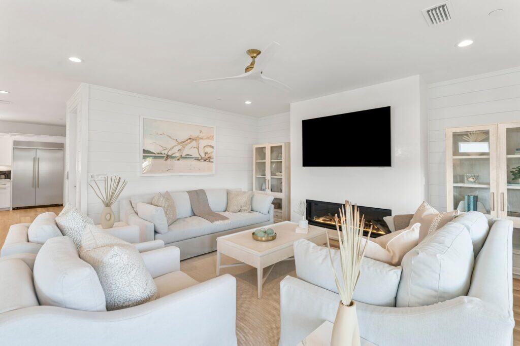 A modern living room with light-colored sofas, a wall-mounted TV, fireplace, and minimalistic decor in a bright, open space.