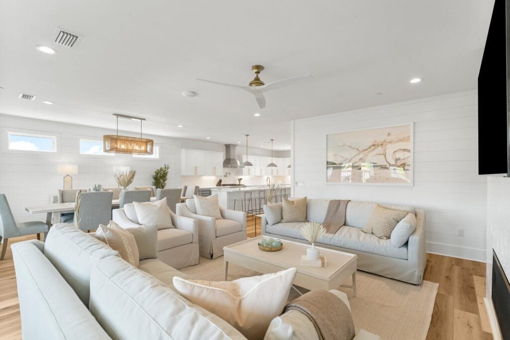 Bright, modern open-plan living area with neutral tones, comfortable seating, a dining table, and a kitchen featuring pendant lights and bar stools.