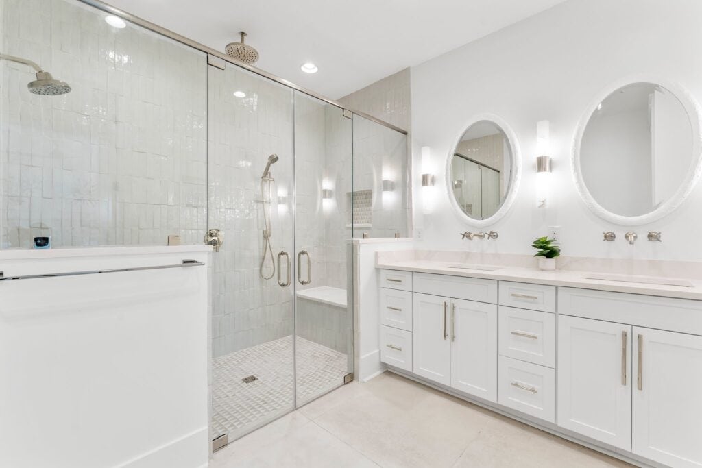 Spacious modern bathroom features double vanity, round mirrors, glass-enclosed shower, and elegant lighting, creating a sleek and refreshing ambiance.