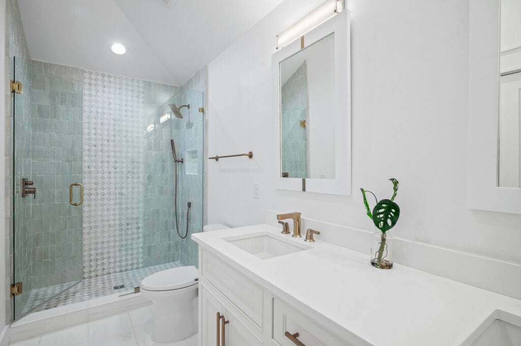Modern bathroom with glass shower, geometric tiled walls, white vanity, large rectangular mirror, and green plant decor. Bright, clean, and minimalistic design.