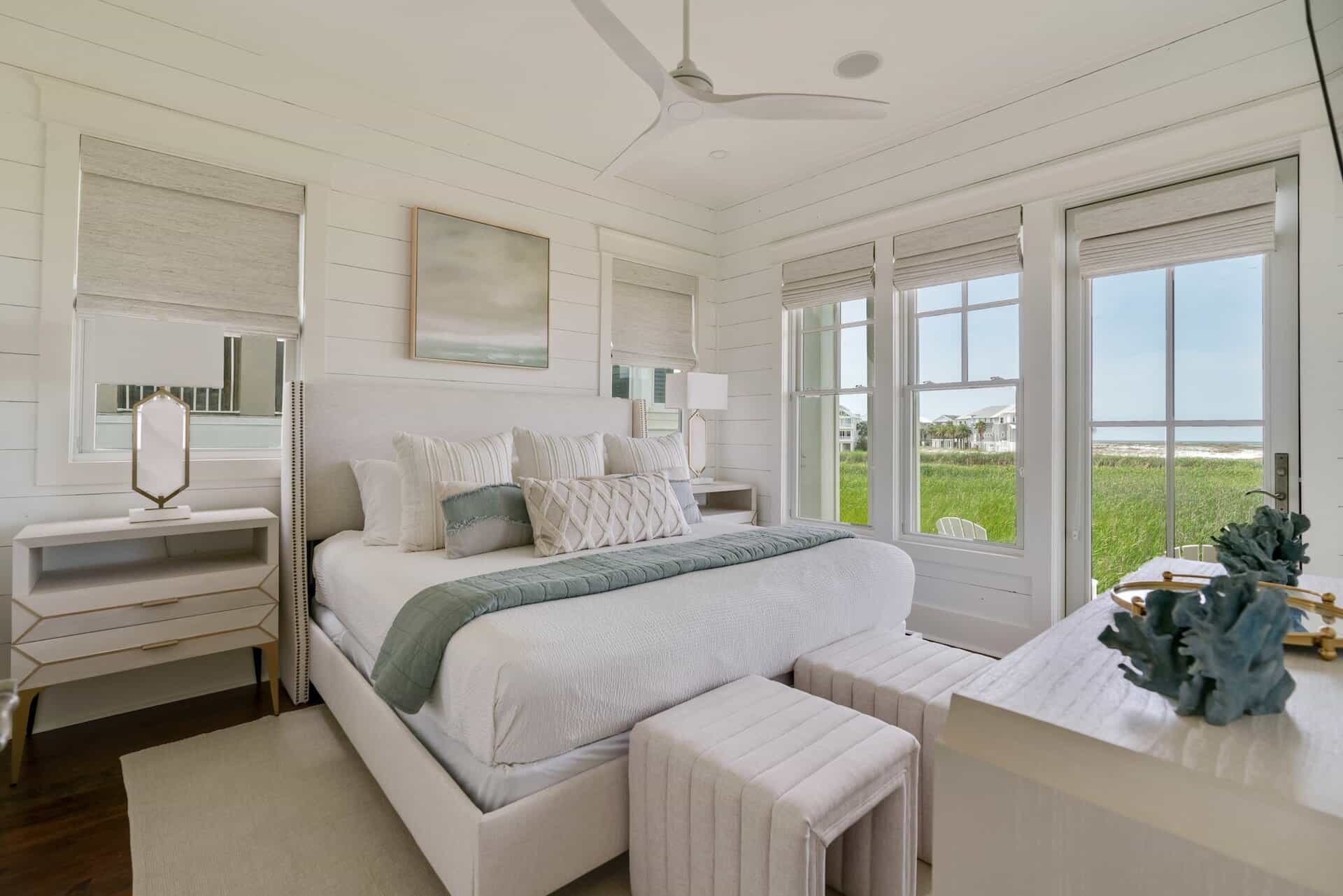 A serene bedroom with coastal decor, white and gray tones, large windows, and ocean view, creates a calm and inviting atmosphere.